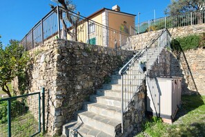 Eine Steintreppe führt zu einem Gebäude mit einem Metallgeländer, einem kleinen Garten und einer Steinmauer.