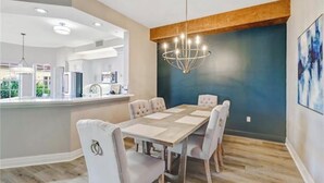 A dining area with a wooden table and chairs, a chandelier, and a view of the kitchen. - Luxury 2 Bed 2 Bath  Penthouse Bayfront Condo off 5th Avenue (Naples)