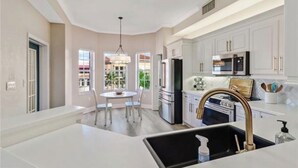 A modern kitchen with white cabinetry, stainless steel appliances, and a central island with a sink. - Luxury 2 Bed 2 Bath  Penthouse Bayfront Condo off 5th Avenue (Naples)
