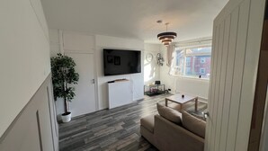 A modern living room with a flat-screen TV, a sofa, a coffee table, and a potted plant.