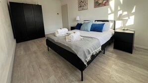 A bedroom with a bed, a nightstand, a lamp, a wardrobe, and two paintings on the wall.