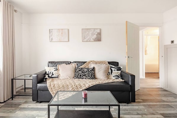 A modern living room with a black leather sofa, a glass coffee table, and two abstract paintings on the wall. - FREE Parking 2-Bedroom Apartment In The Centre of Wimbledon! (London)