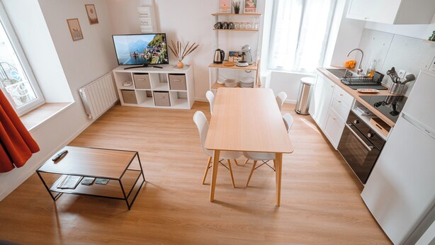 A modern kitchen with white cabinets, a wooden dining table, and a built-in oven. - Charming T2 in the center of Saint-Astier (Saint-Astier)