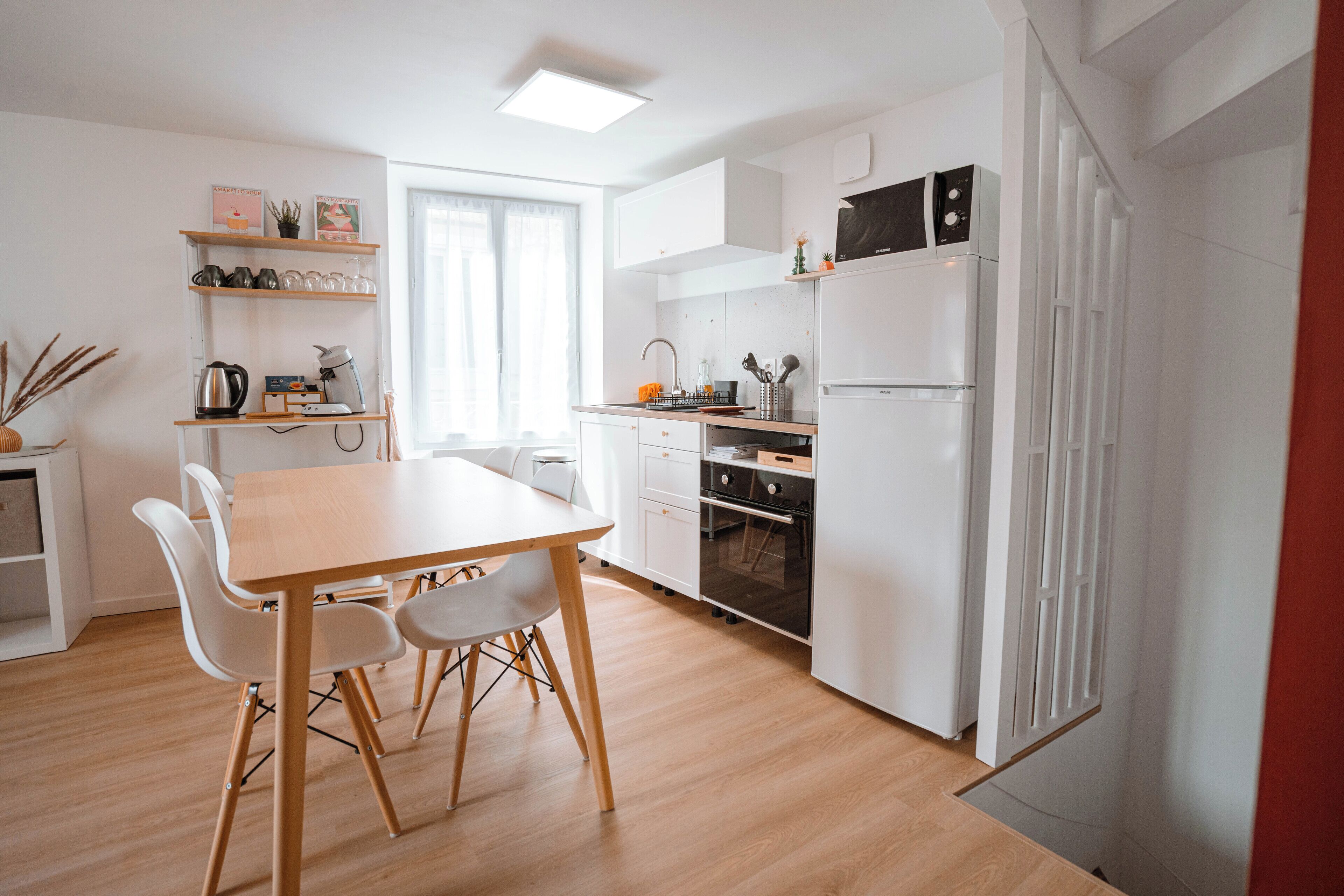 Una cucina moderna con mobili bianchi, forno integrato e frigorifero. C'è un tavolo da pranzo con sedie e una finestra che offre luce naturale.