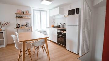 Una cucina moderna con mobili bianchi, forno integrato e frigorifero. C'è un tavolo da pranzo con sedie e una finestra che offre luce naturale.
