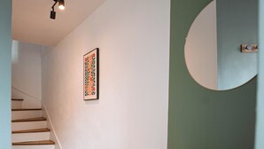 A hallway with a wooden staircase, a white cabinet, and a wall-mounted mirror. - Charming T2 in the center of Saint-Astier (Saint-Astier)