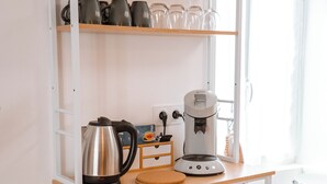 A kitchen with a coffee maker, a kettle, and a shelf with plates and cups. - Charming T2 in the center of Saint-Astier (Saint-Astier)