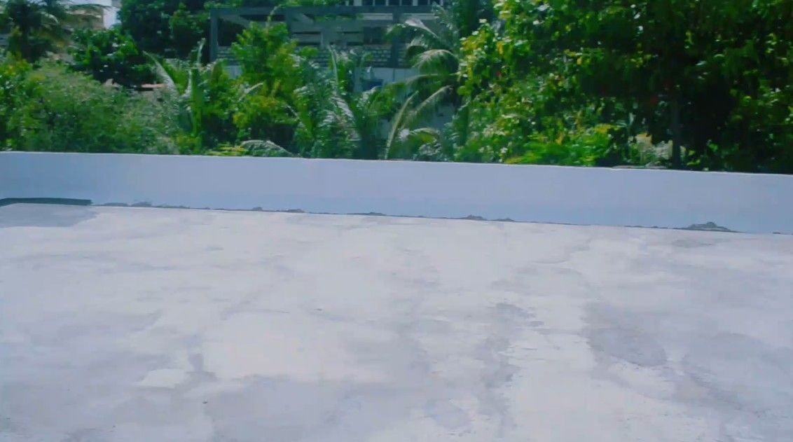 Un toit-terrasse avec une surface en béton, entouré de verdure et avec des bâtiments en arrière-plan.