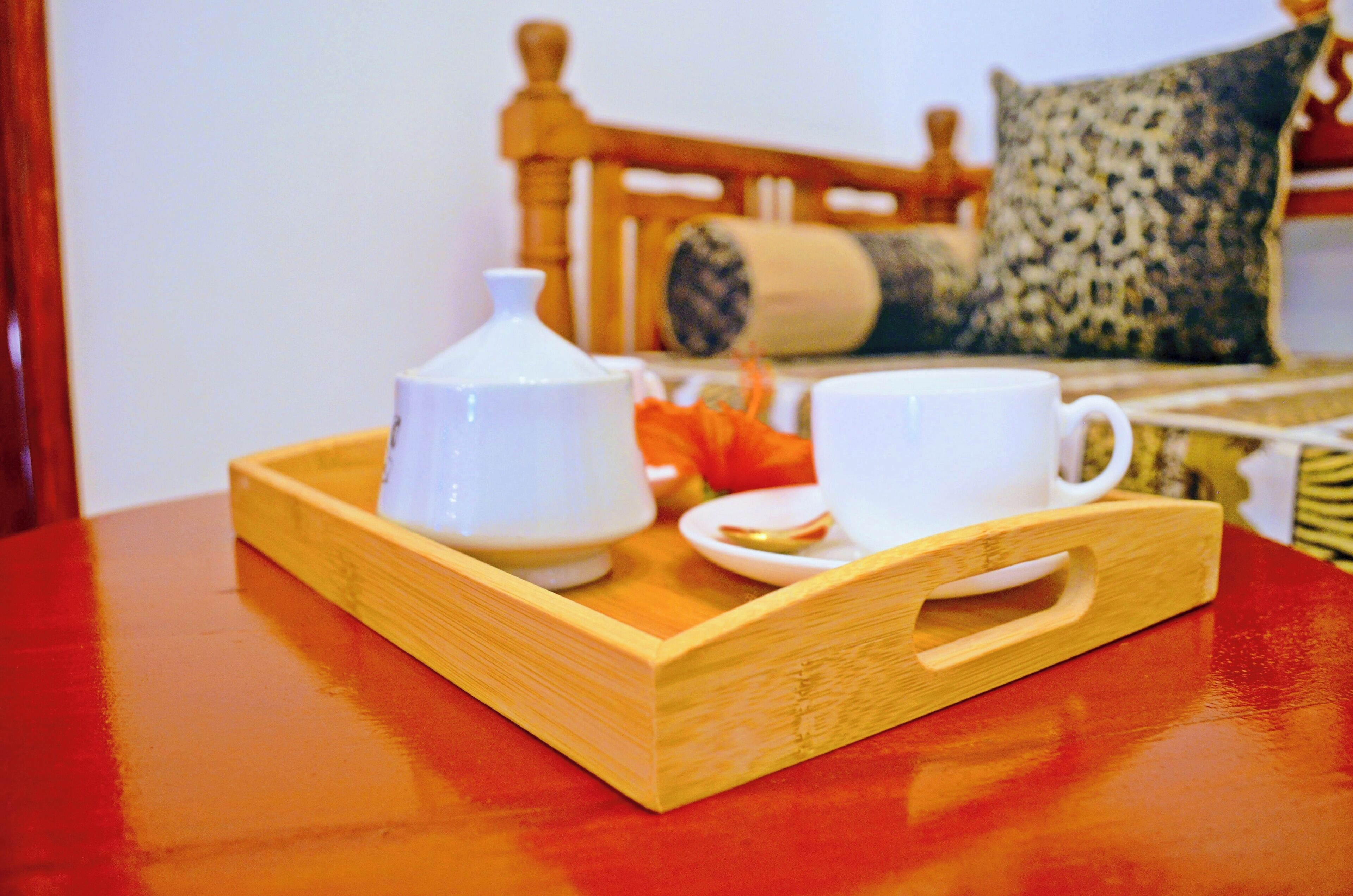Una bandeja de madera con una tetera blanca, una taza blanca y un plato con comida sobre una mesa roja.