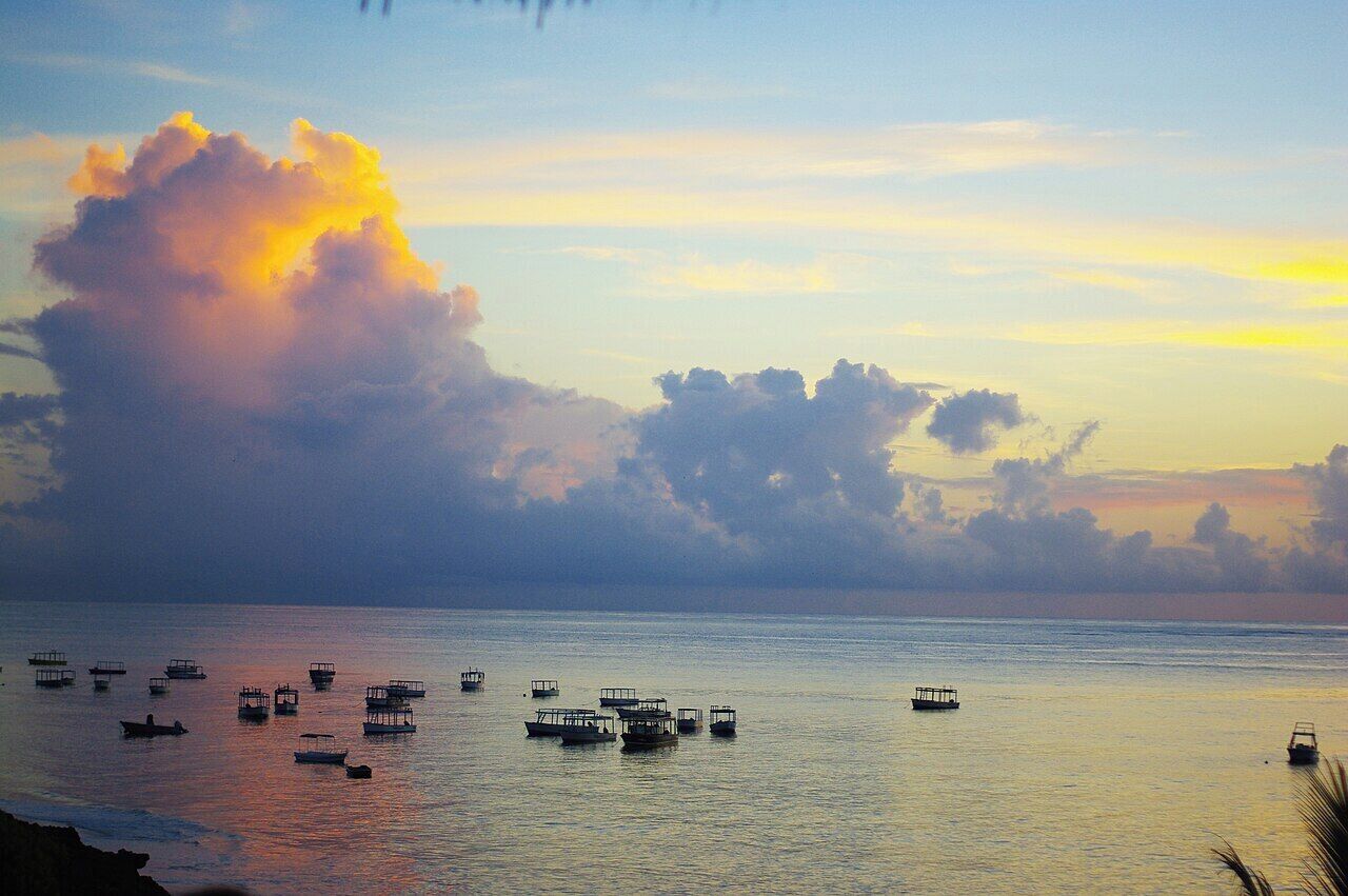 A calm sea with several boats and a large cloud formation.