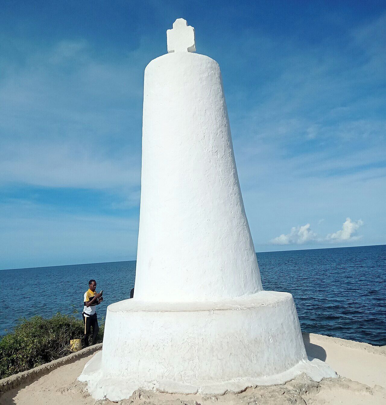 A white lighthouse by the sea with a clear sky.