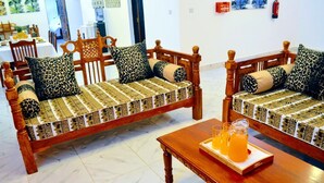 Zwei Holzsofas mit gemusterten Kissen, ein Holztisch mit einer Getränkeauswahl und ein Fliesenboden.