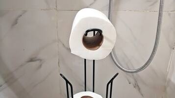 A toilet paper holder in a bathroom with marble walls and a shower hose.