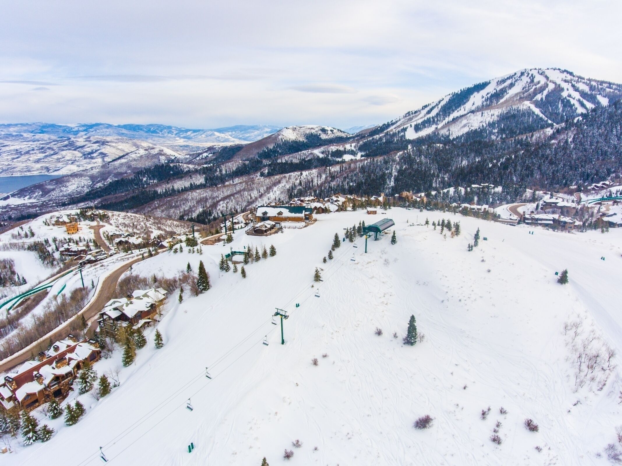 A snow-covered ski resort with a mountain backdrop, ski lifts, and a lodge with multiple buildings.