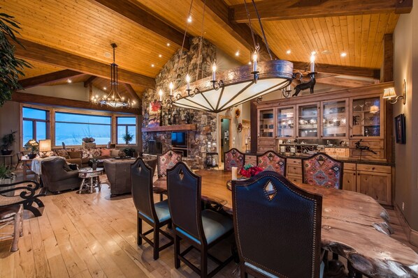 A spacious living room with a large wooden dining table, comfortable seating, and a stone fireplace. - Majestic Ski in Ski Out Estate (Park City)