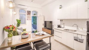 A modern kitchen with white cabinets, a dining area with a glass table, and a TV on a wooden stand. - Machane Yehuda 2 - One Bedroom Apartment, Sleeps 4 (Jerusalem)