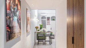 A hallway with a wooden door, a dining area with a table and chairs, and artwork on the walls. - Machane Yehuda 2 - One Bedroom Apartment, Sleeps 4 (Jerusalem)