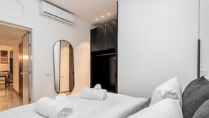 A modern hotel room with a neatly made bed, a large mirror, a wardrobe, and an air conditioning unit. - Machane Yehuda 2 - One Bedroom Apartment, Sleeps 4 (Jerusalem)