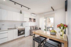 Une cuisine moderne avec des armoires blanches, un four encastré et un coin repas comprenant une table en verre et des tabourets de bar noirs.
