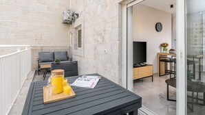 Un balcon avec une table où sont disposés un plateau contenant du jus d’orange, un journal et une petite plante.