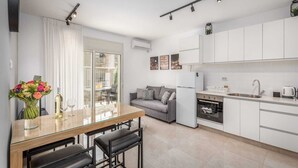 Une cuisine moderne avec des meubles blancs, un coin repas doté d’une table en verre et un canapé gris.