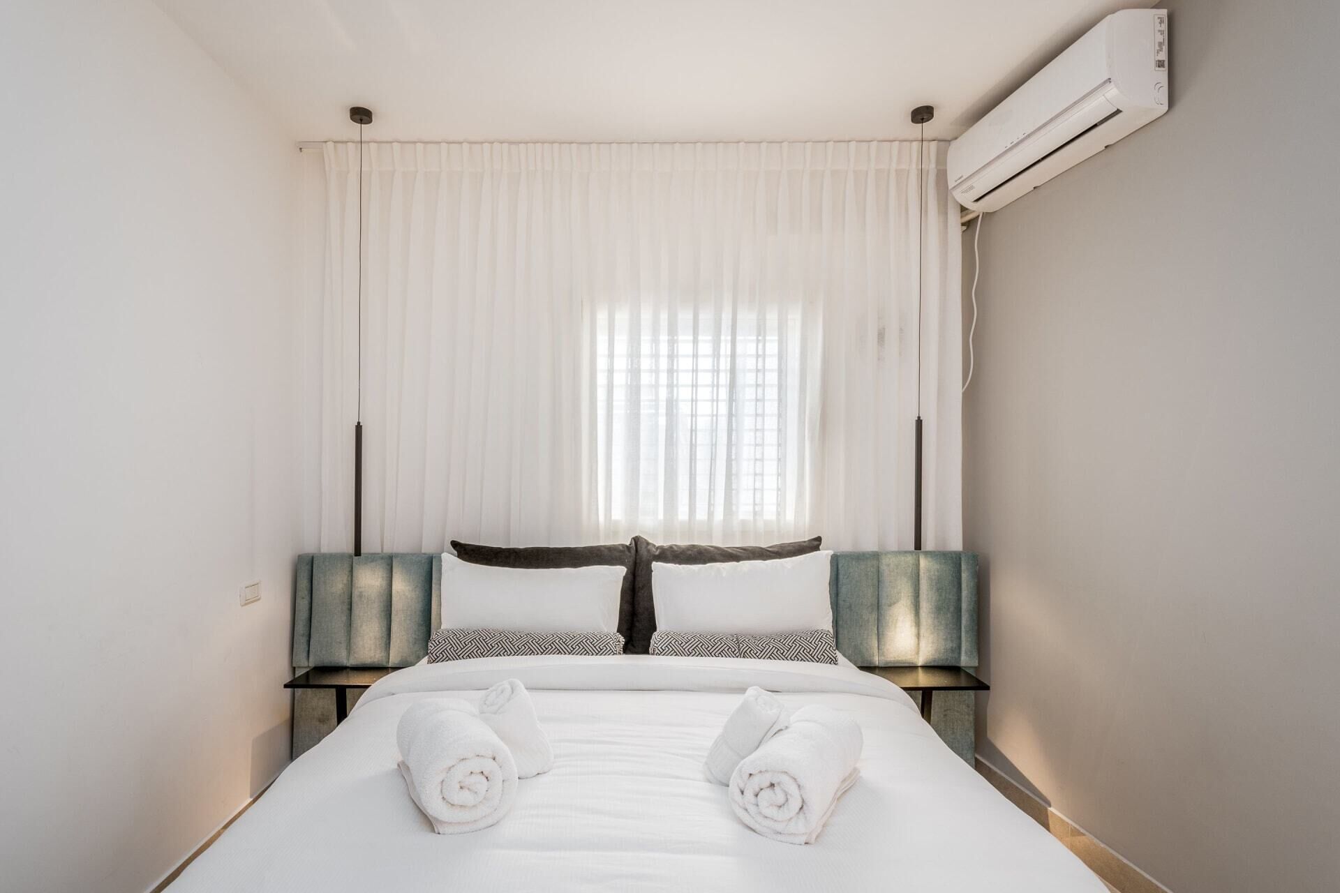 Ein Hotelzimmer mit einem Bett, weißen Vorhängen, einer Klimaanlage und zwei Nachttischen mit Lampen.