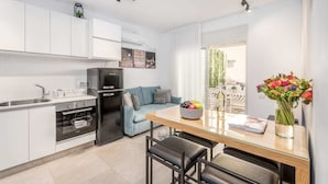 A modern kitchen with white cabinets, a black refrigerator, and a dining area with a glass table and black chairs. - Machane Yehuda 4 - One Bedroom Apartment, Sleeps 4 (Jerusalem)