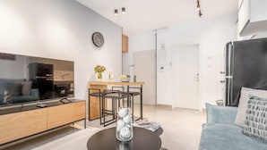 A modern living room with a flat-screen TV, a coffee table with decorative items, a sofa, and a dining area with a wooden table and chairs. - Machane Yehuda 4 - One Bedroom Apartment, Sleeps 4 (Jerusalem)