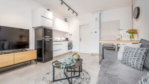 A modern living room with a grey sofa, a coffee table with a vase, and a TV on a wooden cabinet. - Machane Yehuda 5 - One Bedroom Apartment, Sleeps 4 (Jerusalem)