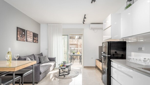 A modern apartment with a kitchen, dining area, and living room. There is a sofa, a dining table, and a coffee table. The kitchen has a refrigerator and a sink. - Machane Yehuda 5 - One Bedroom Apartment, Sleeps 4 (Jerusalem)