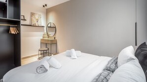 A modern hotel room with a neatly made bed, a small vanity with a mirror, and a wardrobe with folded towels. - Machane Yehuda 5 - One Bedroom Apartment, Sleeps 4 (Jerusalem)
