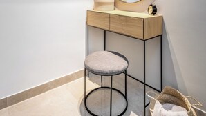 A modern bathroom with a vanity, a round mirror, a stool, and a shelf with decorative items. - Machane Yehuda 5 - One Bedroom Apartment, Sleeps 4 (Jerusalem)
