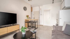A modern living room with a flat-screen TV, a coffee table with a plant, a sofa, and a kitchen area with a fridge and a sink. - Machane Yehuda 6 - One Bedroom Apartment, Sleeps 4 (Jerusalem)