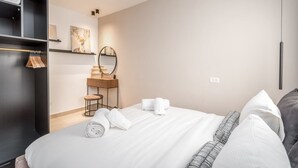 Une chambre d’hôtel comprenant un lit, une coiffeuse avec un miroir, une étagère avec des serviettes et un appareil de climatisation.