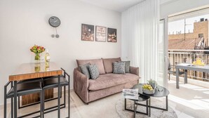 Un salon moderne avec un canapé, une table à manger et une table basse. Des tableaux encadrés ornent le mur, et une horloge y est également accrochée.