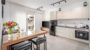 Une cuisine moderne avec un coin repas, comprenant une table en verre, des tabourets de bar noirs et un réfrigérateur.