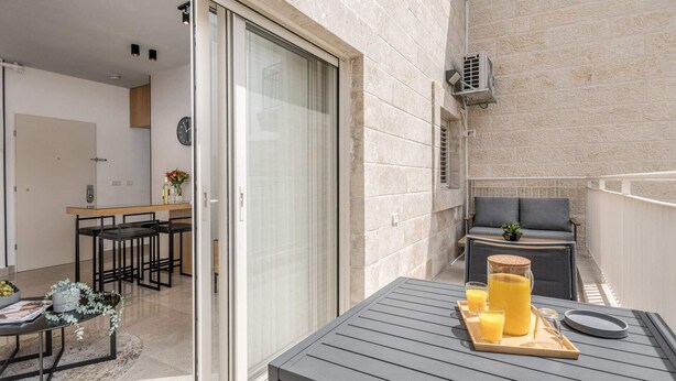 En balkon med et bord dækket til morgenmad, en sofa og en potteplante.