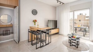 Et moderne hotelværelse med spiseplads, tv, vækkeur og en balkon med bord og stole.