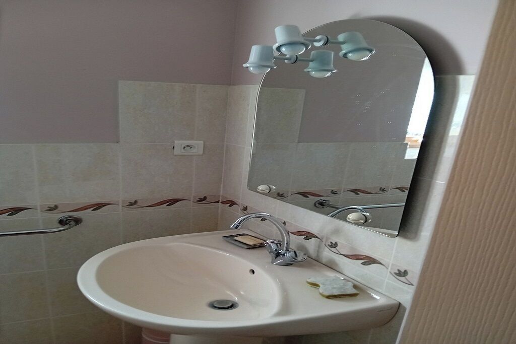 A bathroom with a sink, mirror, and handrail.
