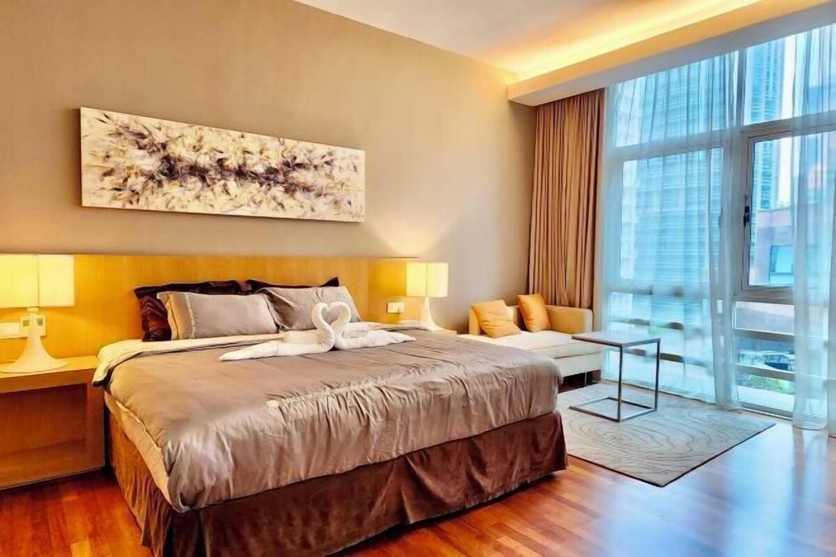 Een moderne hotelkamer met een groot bed, twee bedlampen, stadszicht door middel van kamerhoge ramen en een groot abstract schilderij aan de muur.