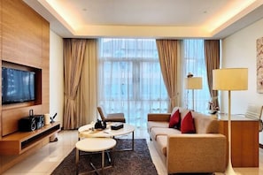 Una habitación de hotel moderna con televisión de pantalla plana, un sofá, una mesa de centro, un escritorio y un ventanal con cortinas.