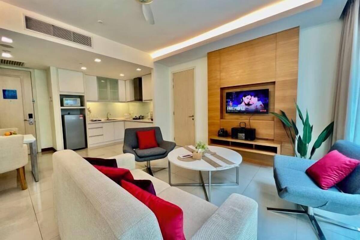 Een moderne woonkamer met een bank, stoelen, een salontafel en een aan de muur bevestigde televisie.