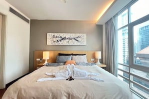 Habitación de hotel con una cama grande, dos lámparas de noche, vistas a la ciudad y un cuadro en la pared.