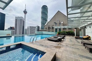 Piscina en la azotea con vista al horizonte de la ciudad, incluyendo una torre y un edificio moderno.