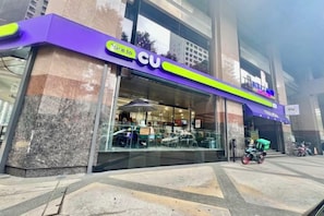 Fachada de tienda CU con vidrio, mesas al aire libre y una motocicleta estacionada fuera.