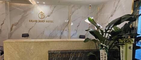 Mostrador de recepción de hotel con una pared de mármol, un logotipo y un cartel que dice 'INFORMACIÓN'.