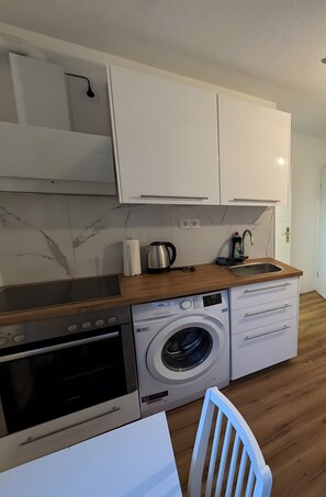 Eine kompakte Küche mit Einbauwaschmaschine, Kaffeemaschine und Mikrowelle.