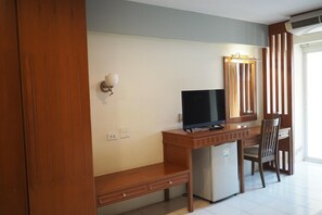 Une chambre d’hôtel compacte comprenant un bureau en bois, une télévision, un petit réfrigérateur, une chaise et un luminaire fixé au mur.