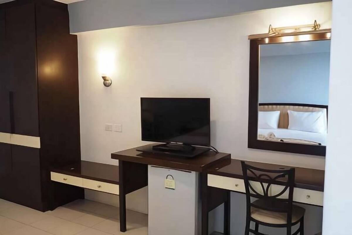 A hotel room with a desk, a television, a mirror, and a wardrobe.