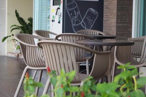 A seating area with chairs and a table, a wall with a soda can illustration, and a potted plant in the foreground. - Phromsuk Hotel Ayutthaya (Phra Nakhon Si Ayutthaya)